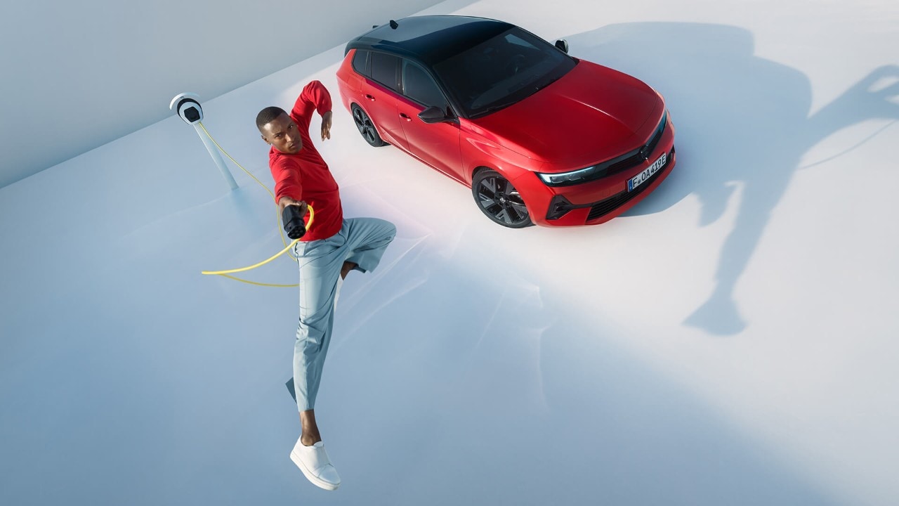 Opel Astra Sports Tourer Electric sedd uppifrån, bredvid hoppar en man med röd tröja med en laddkabel i handen