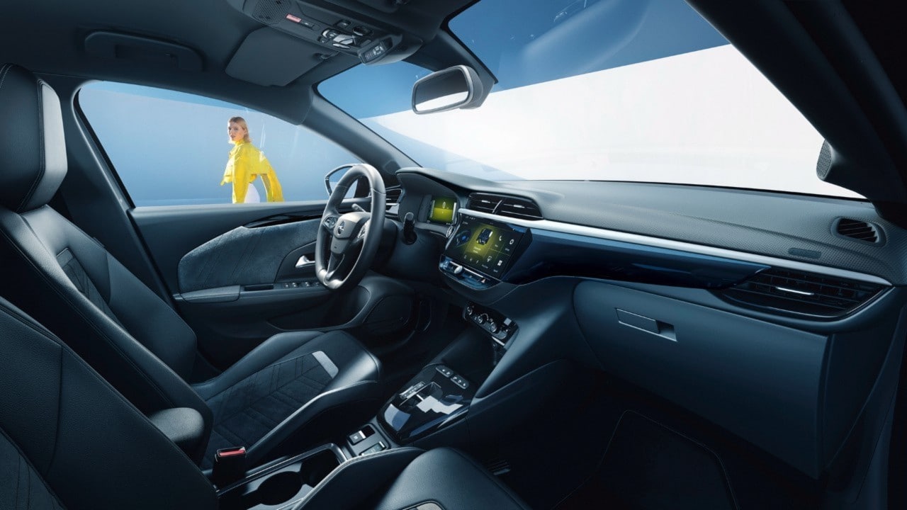 Svart interiör i Opel Corsa Electric sedd från passagerarsäten med en kvinna med gul jacka i bakgrunden
