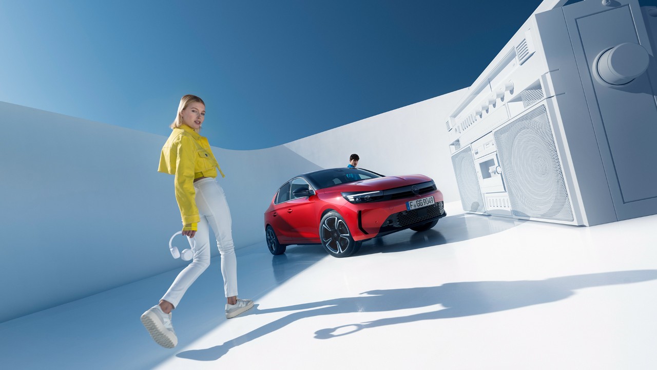 Kvinna med gul jacka går framför röd Opel Corsa